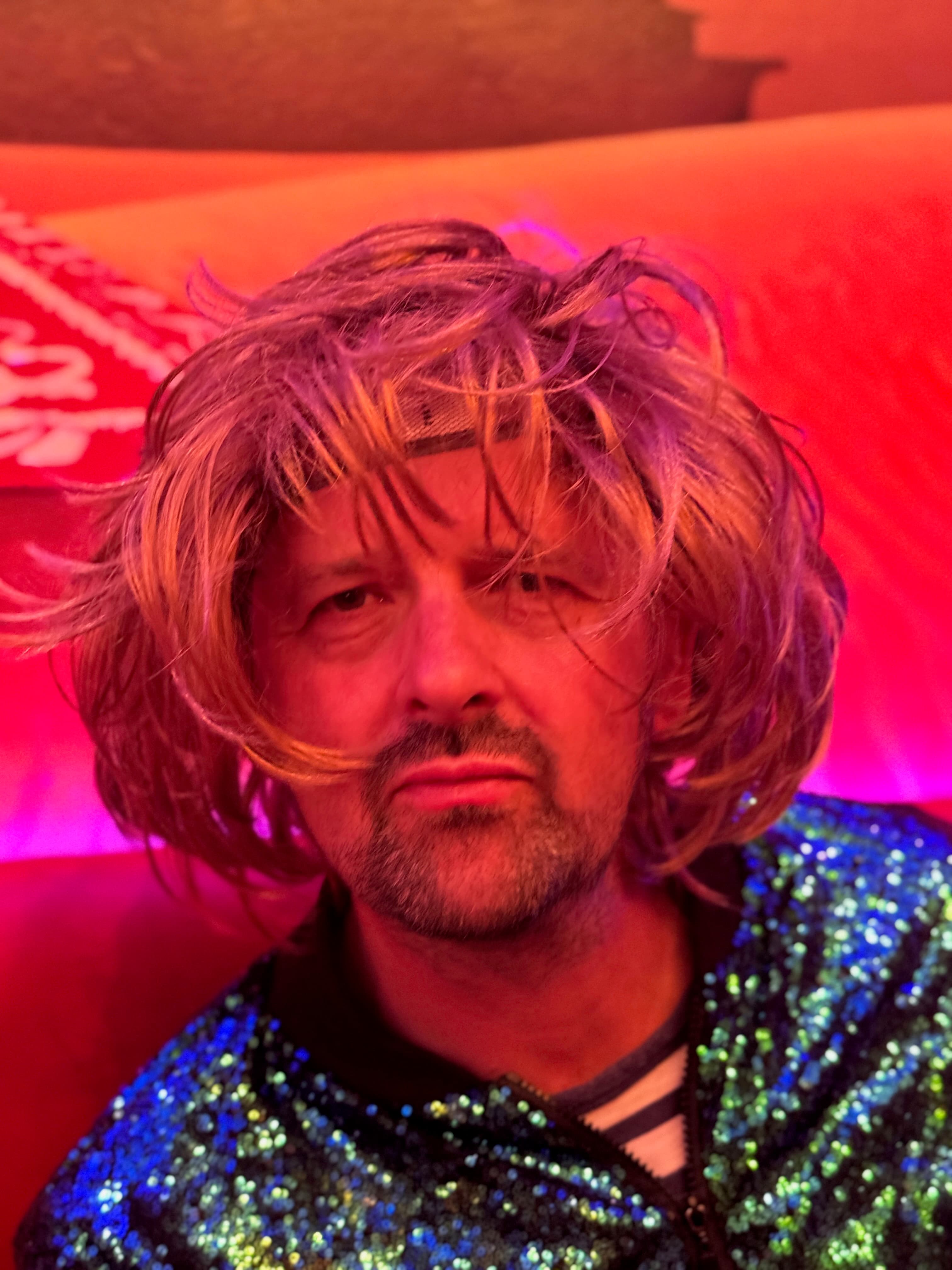 Red-lit close-up of a guest in a wig at the party
