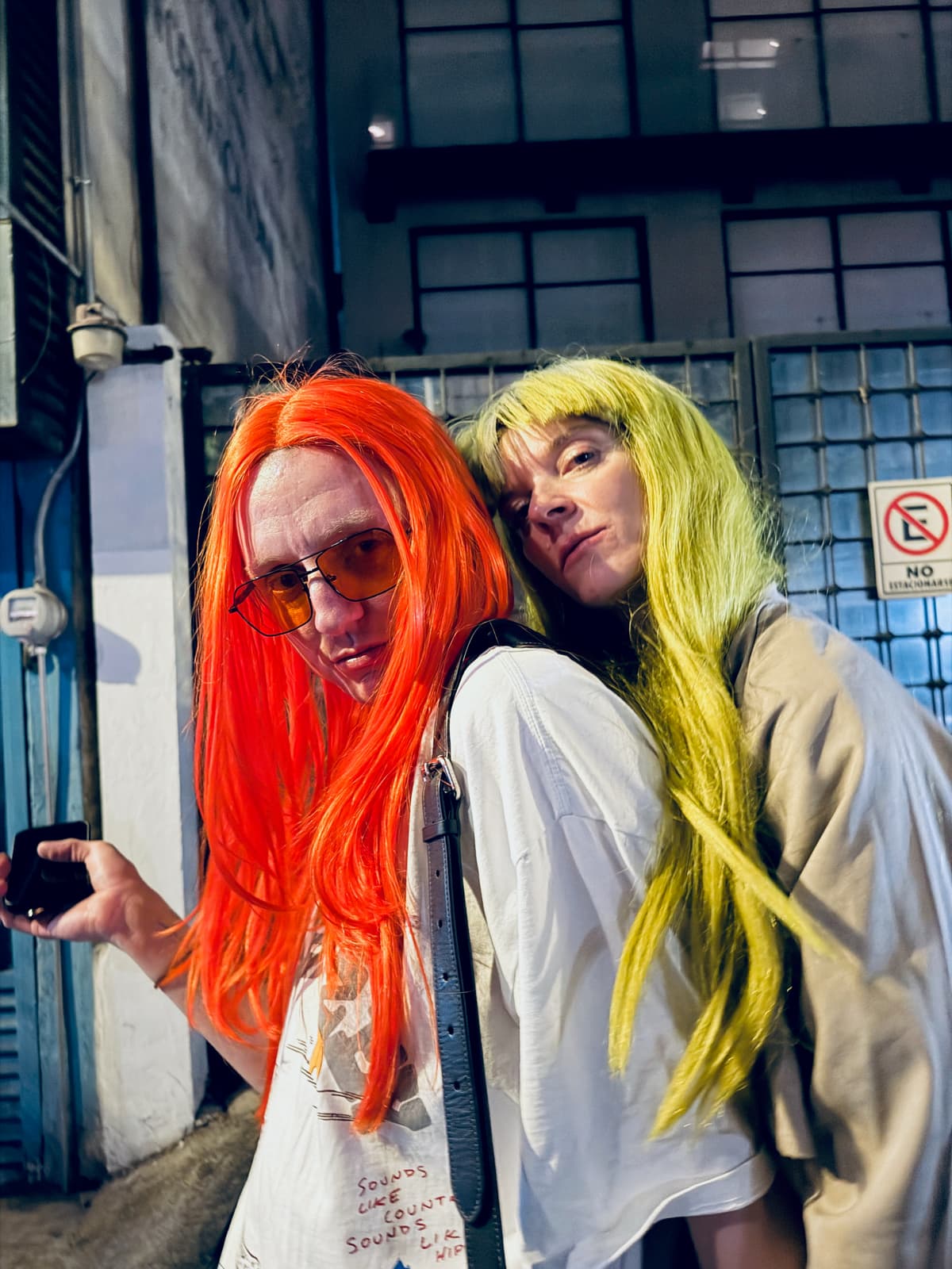 Two friends in orange and lime wigs posing outside at night