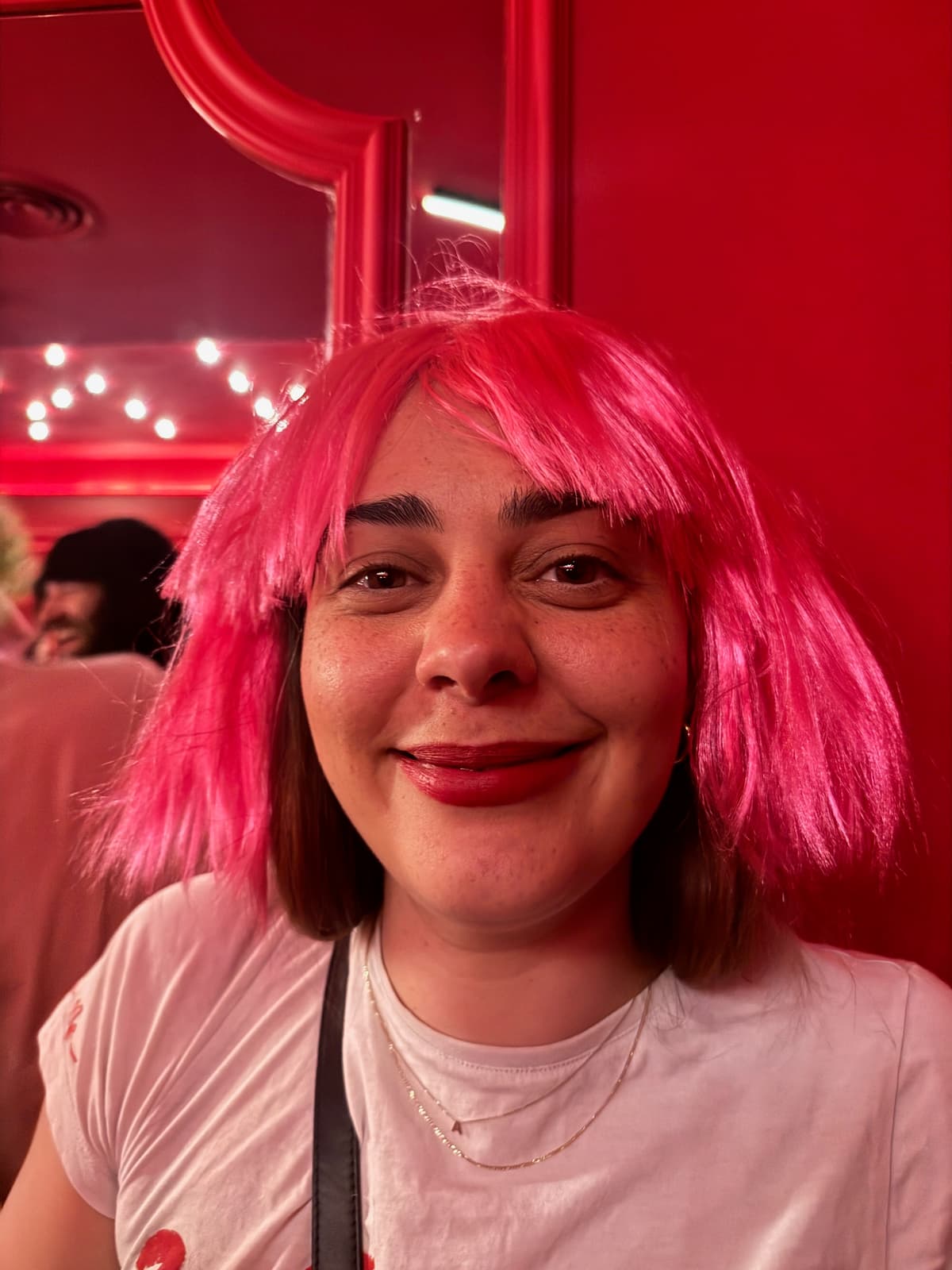 Close-up portrait of a smiling person in a bright pink wig under red party lighting