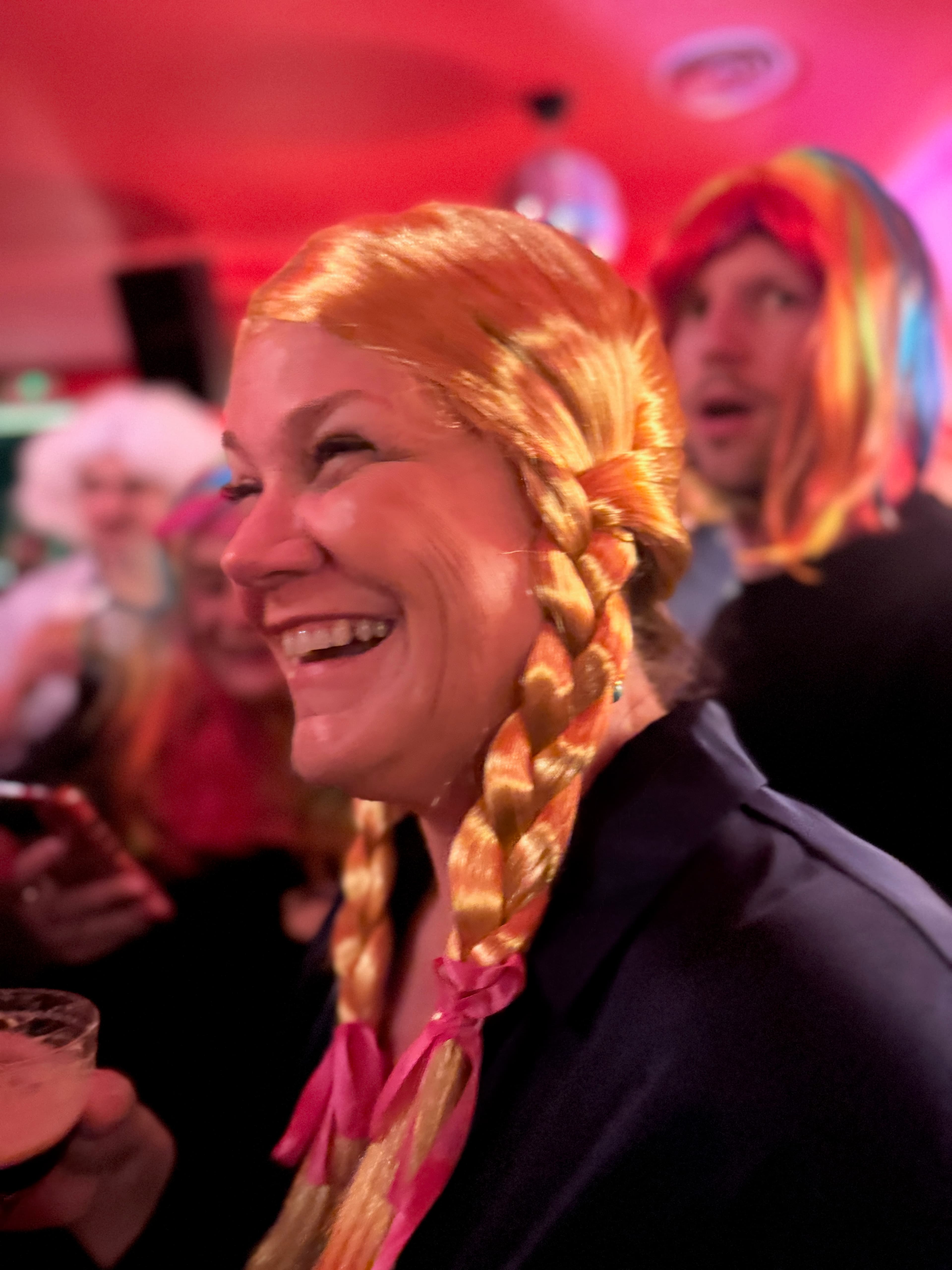 Laughing party guest in a blonde braided wig holding a drink